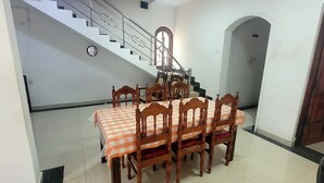 A dining area with a checkered tablecloth, wooden chairs, a staircase, and a ceiling fan. - Grace- The Joyful Rest (Batticaloa)