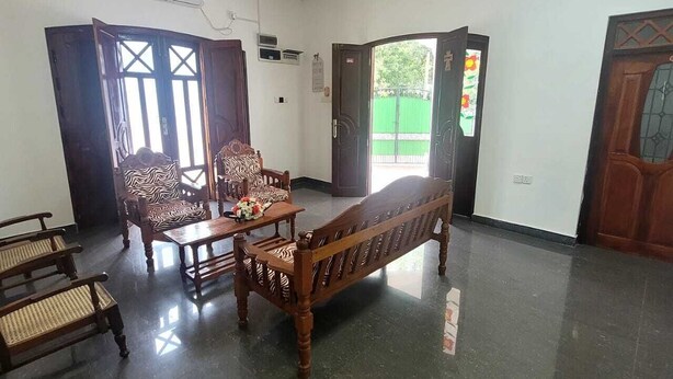 A room with a ceiling fan, a wooden sofa, a zebra-patterned chair, a small table with flowers, and a green view outside. - Grace- The Joyful Rest (Batticaloa)