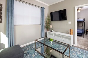 Un salon avec une table basse en verre, un téléviseur à écran plat fixé au mur, un meuble de rangement blanc et un tapis bleu à motifs.