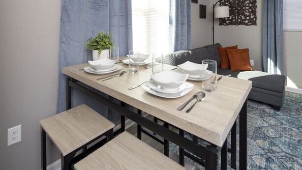 Un coin repas avec une table en bois dressée pour quatre personnes, des bancs et un canapé gris en arrière-plan.