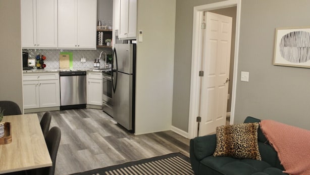 A compact kitchen with white cabinets, stainless steel appliances, and a dining area with a table and chairs. - Relax & Explore Downtown Little Rock (Little Rock)