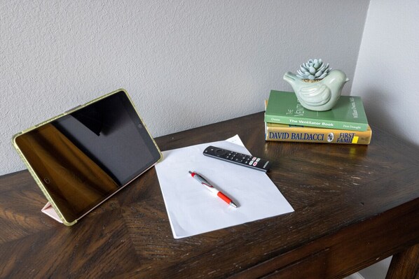 Una mesa de madera con una tableta, un control remoto, un bolígrafo y una pila de libros.