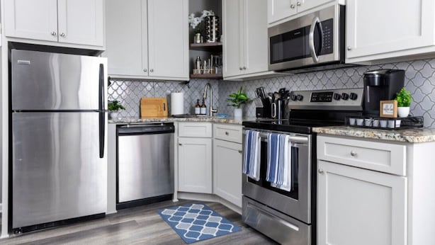 Una cucina moderna con elettrodomestici in acciaio inossidabile, mobili bianchi e una parete di fondo decorata.