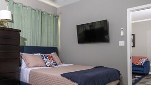 Una camera da letto con un letto, una cassettiera, una televisione e una porta che dà su un'altra stanza.