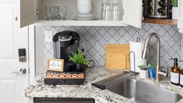A kitchen with white cabinets, a granite countertop, a coffee bar, a sink, and various kitchen appliances.