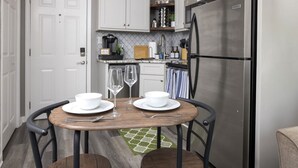 A compact kitchen with a dining table set for two, featuring a stainless steel refrigerator and a coffee maker on the countertop.