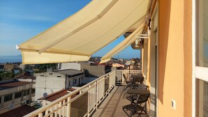 A balcony with a retractable awning, outdoor furniture, and a view of the cityscape. - Luxurious B&B_Junior Suite Black room (Palmi)