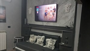 A modern bedroom with a large flat-screen TV mounted on the wall, a black sofa with patterned cushions, a small bedside table, and a marble-patterned wall. - Luxurious B&B_Junior Suite Black room (Palmi)