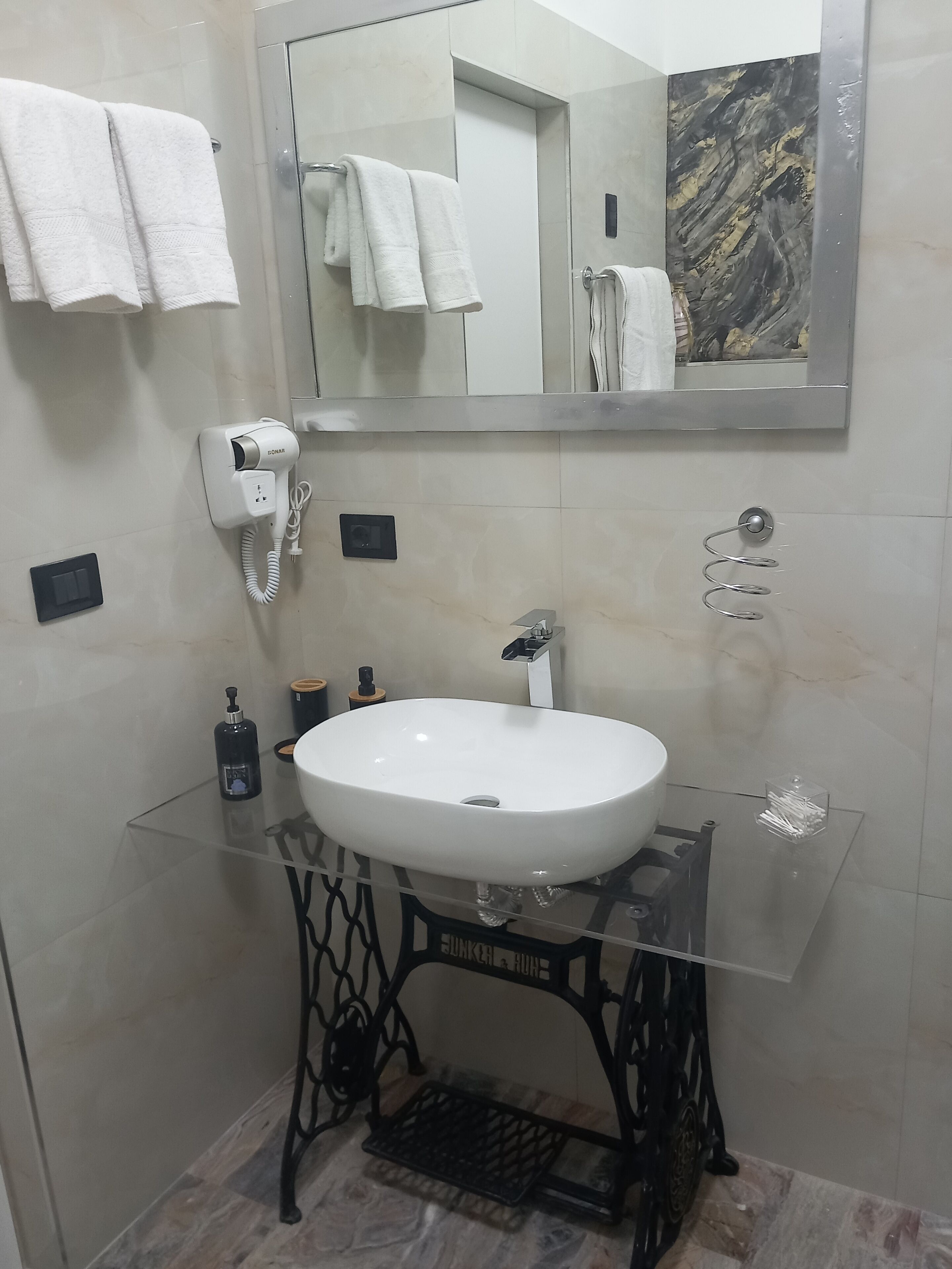 Een badkamer met een wit wastafeltje, een spiegel en een handdoekhouder.