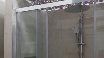 A glass-enclosed shower with a handheld showerhead and a wall-mounted rain showerhead.