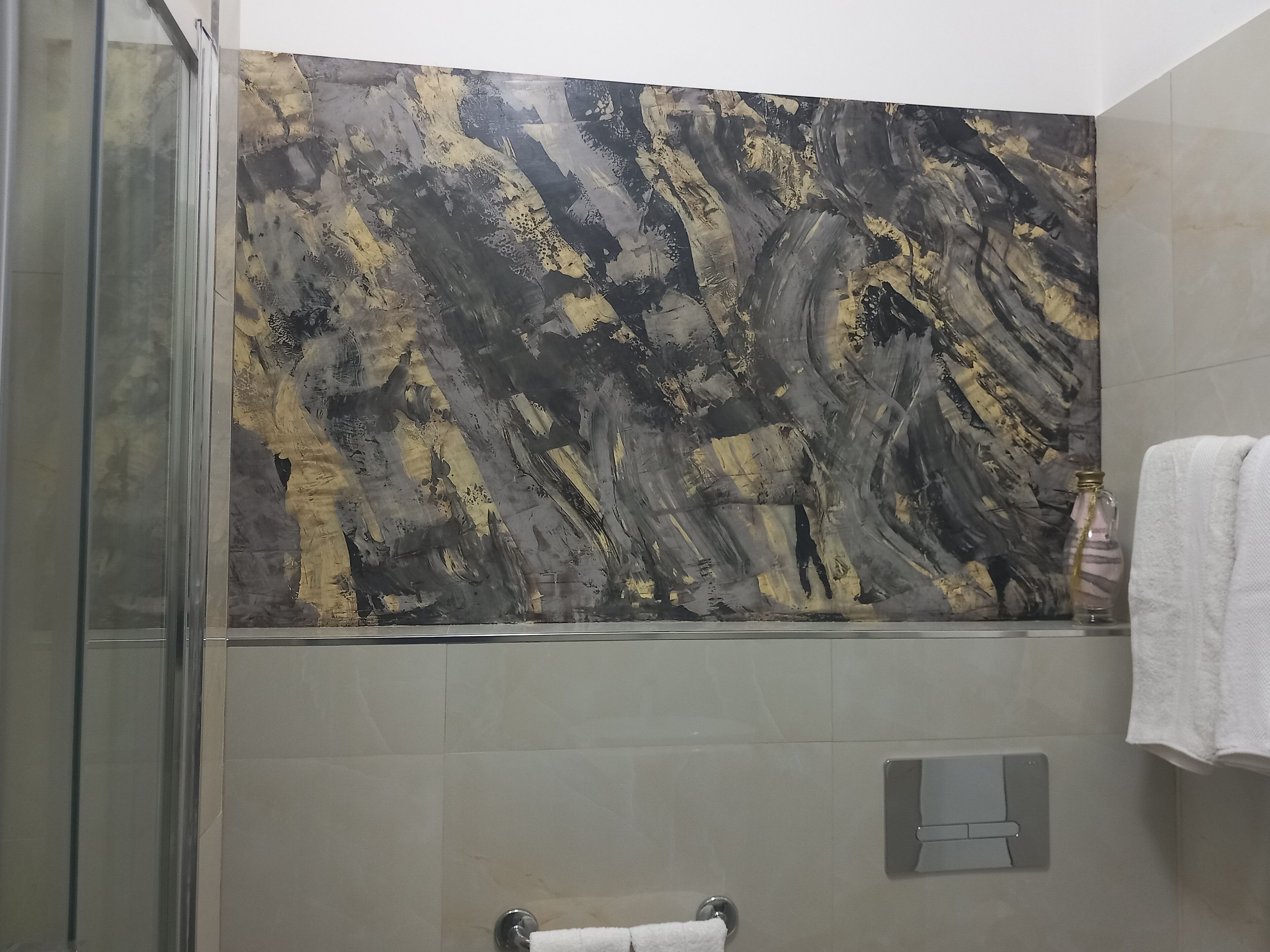 A modern bathroom with a glass shower enclosure, a marble wall with abstract patterns, and a white towel hanging on a rack.