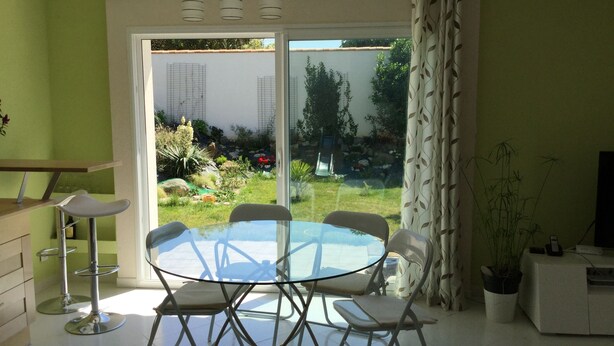 Een moderne keuken met een glazen eettafel en stoelen, een witte kast en een schuifpui naar een tuin.