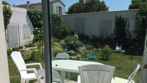 Een terras met witte plastic stoelen en een tafel, omgeven door een tuin met diverse planten en een klein vijvertje.