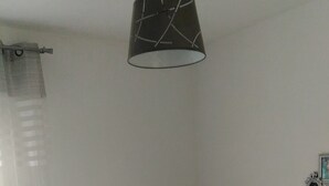 Een slaapkamer met een bed, een hanglamp, een gordijn en een klein decoratief object aan de muur.