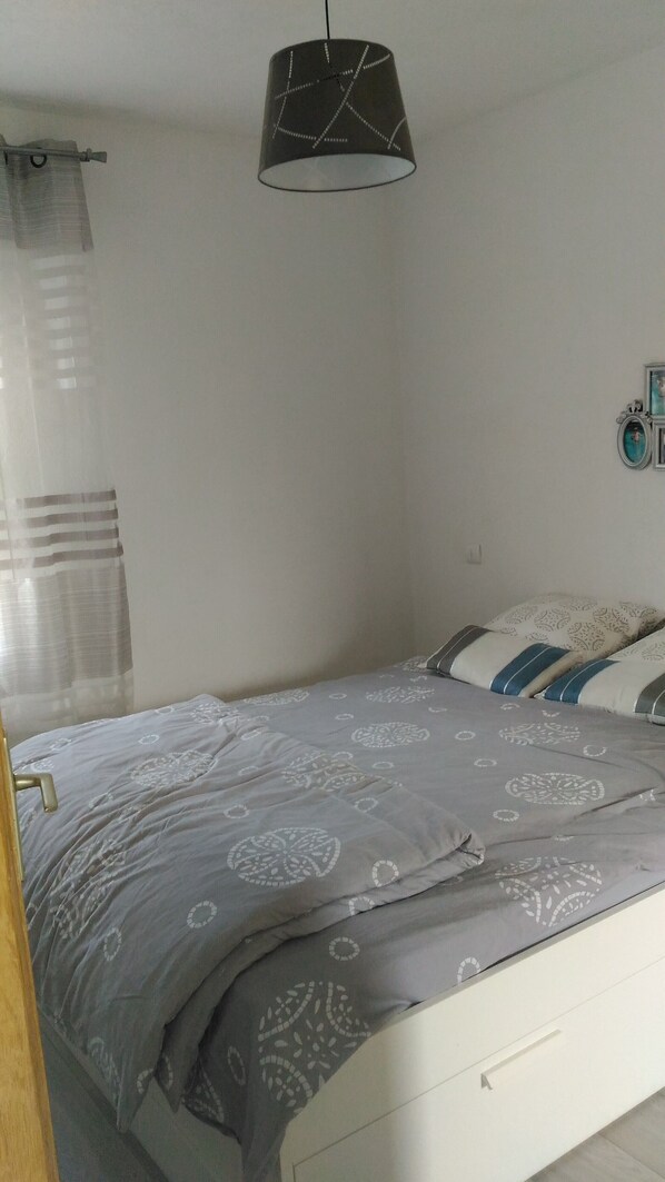 Ein Schlafzimmer mit einem Bett, einer Hängelampe, einem Vorhang und einem kleinen Wanddekor.