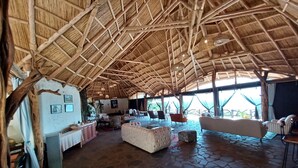 Una habitación amplia con techo de paja, suelo de piedra y asientos cómodos.