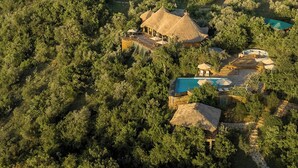 Un resort con edificios de techo de paja, una piscina y exuberante vegetación.