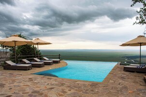 Piscina con sillones de playa y sombrillas, rodeada de suelo de piedra, con vistas a un paisaje pintoresco.