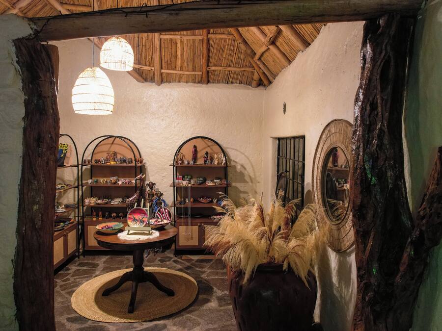 A rustic interior with a round table, shelves with various items, and a large vase with dried plants.