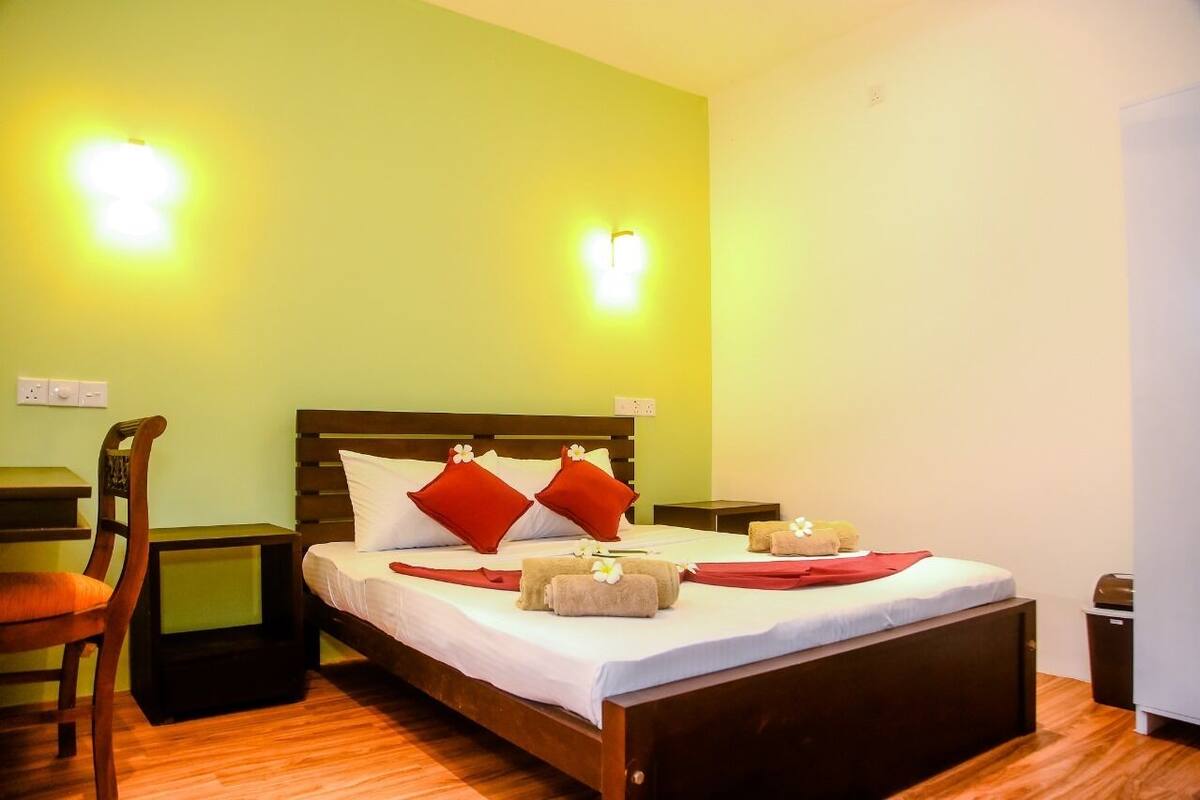Una habitación de hotel con una cama de madera, dos mesitas de noche, una silla y un escritorio pequeño.
