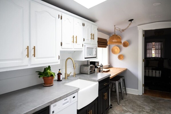 A modern kitchen with white cabinets, gold handles, a built-in microwave, and a coffee maker.