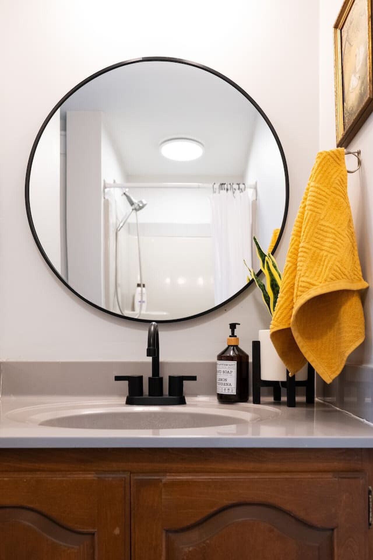 Une salle de bain avec un miroir rond, un lavabo, une serviette jaune et un flacon de savon.