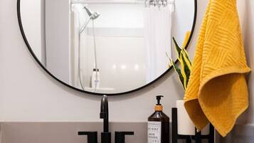 Une salle de bain avec un miroir rond, un lavabo, une serviette jaune et un flacon de savon.