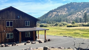 A rustic wooden cabin with a covered porch, situated in a mountainous area with a clear sky.