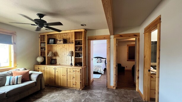 A spacious living area with a wooden cabinet, a ceiling fan, and a view into a bedroom through an open doorway.