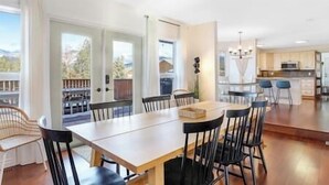 A modern kitchen with a dining area, featuring a large table and chairs, a view through the glass door, and a kitchen island with stools.