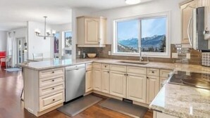 A modern kitchen with a large window, wooden cabinets, and a stainless steel dishwasher.