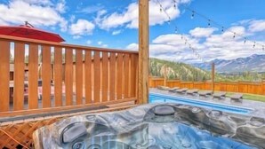 A hot tub with a mountain view, wooden fence, and string lights.