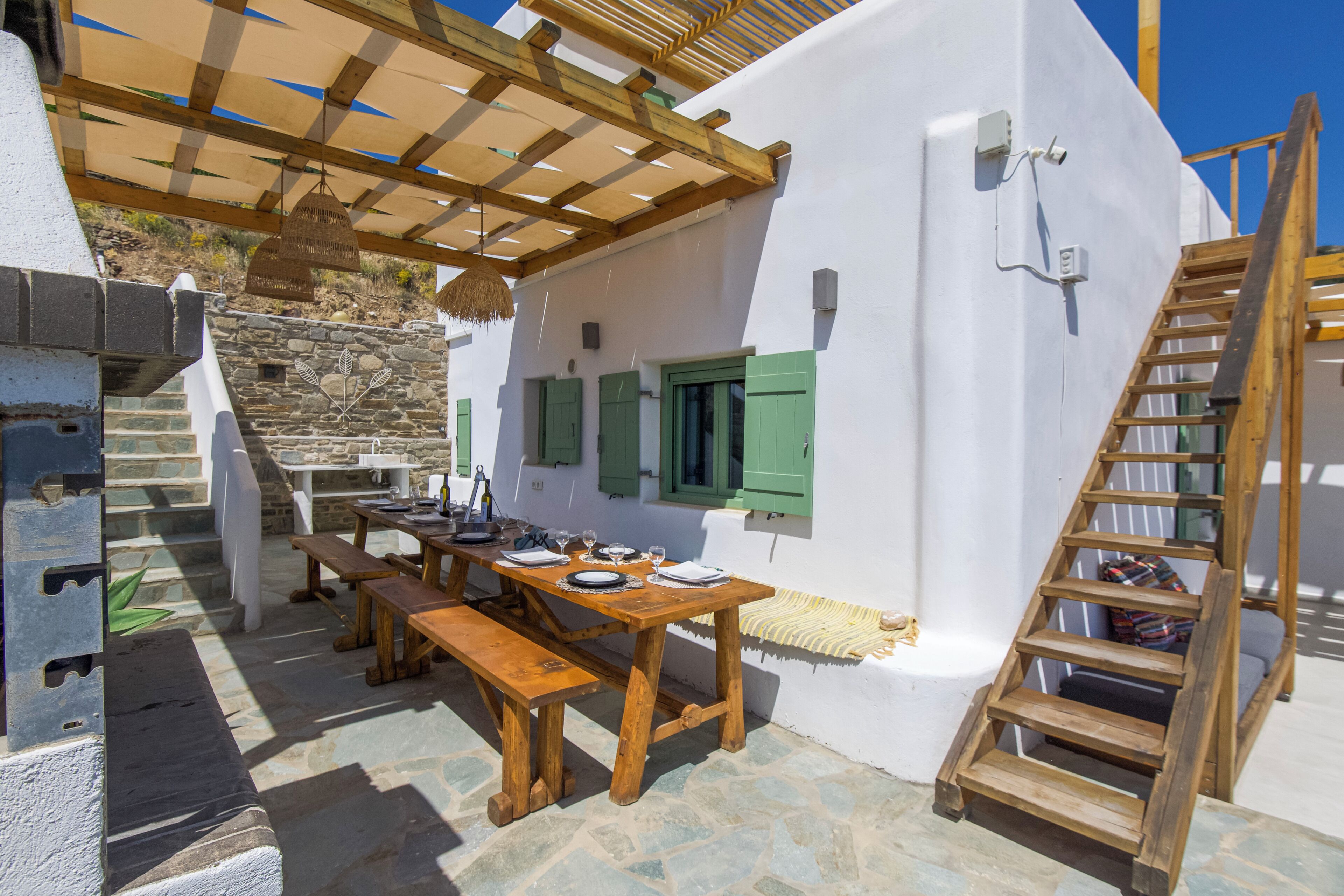 An outdoor dining area with wooden tables and benches, a stone wall, and a wooden ladder.