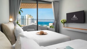 A hotel room with a bed, a TV, a balcony with a view of the ocean and buildings, and a sign on the wall. - Seaside Boutique Hotel Nha Trang Beach (Nha Trang)