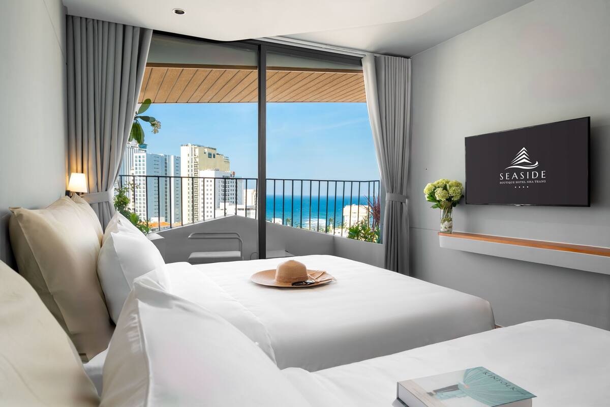 A hotel room with a bed, a TV, a balcony with a view of the ocean and buildings, and a sign on the wall.