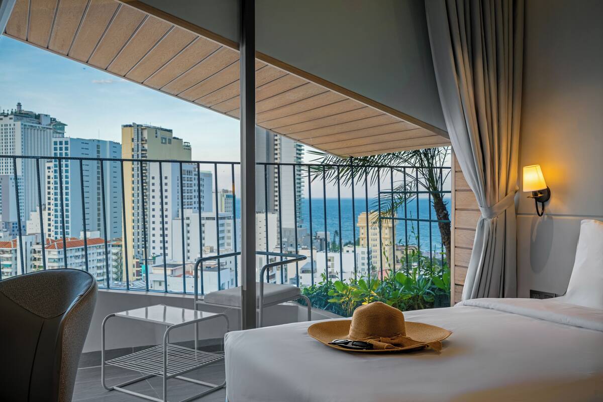 A hotel room with a balcony, a bed, a chair, and a view of the city and ocean.