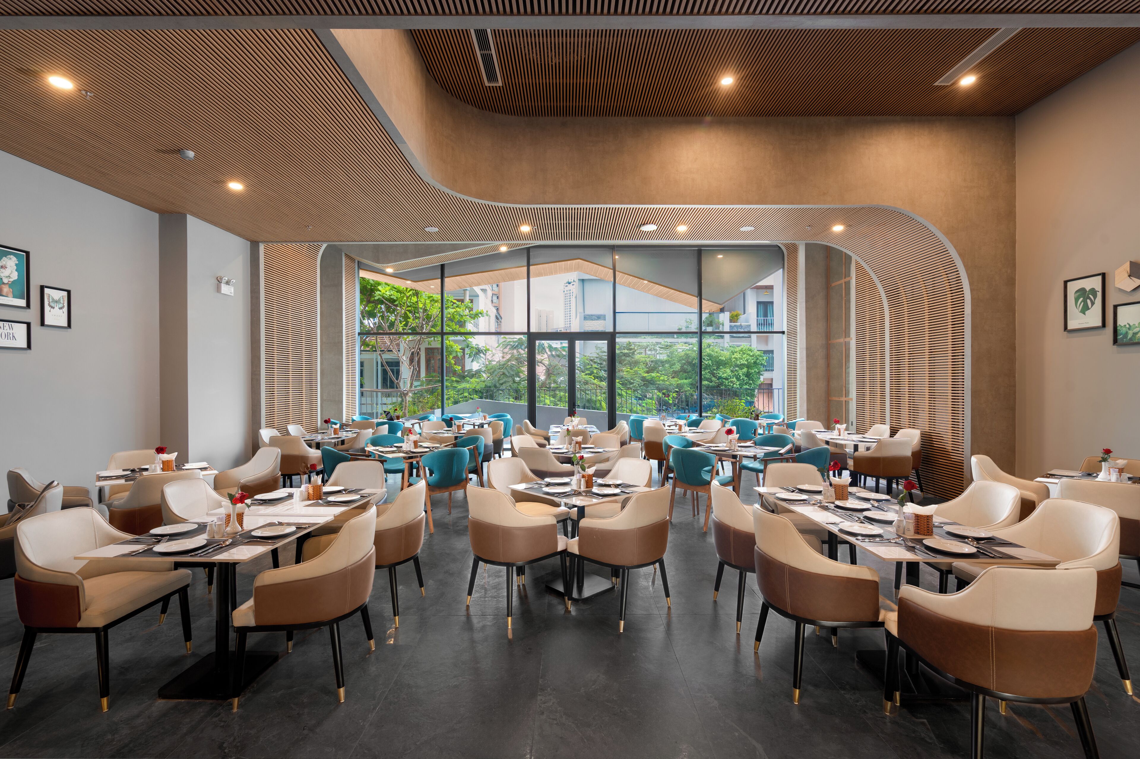 A modern dining area with multiple tables and chairs, large windows offering a view of greenery outside.