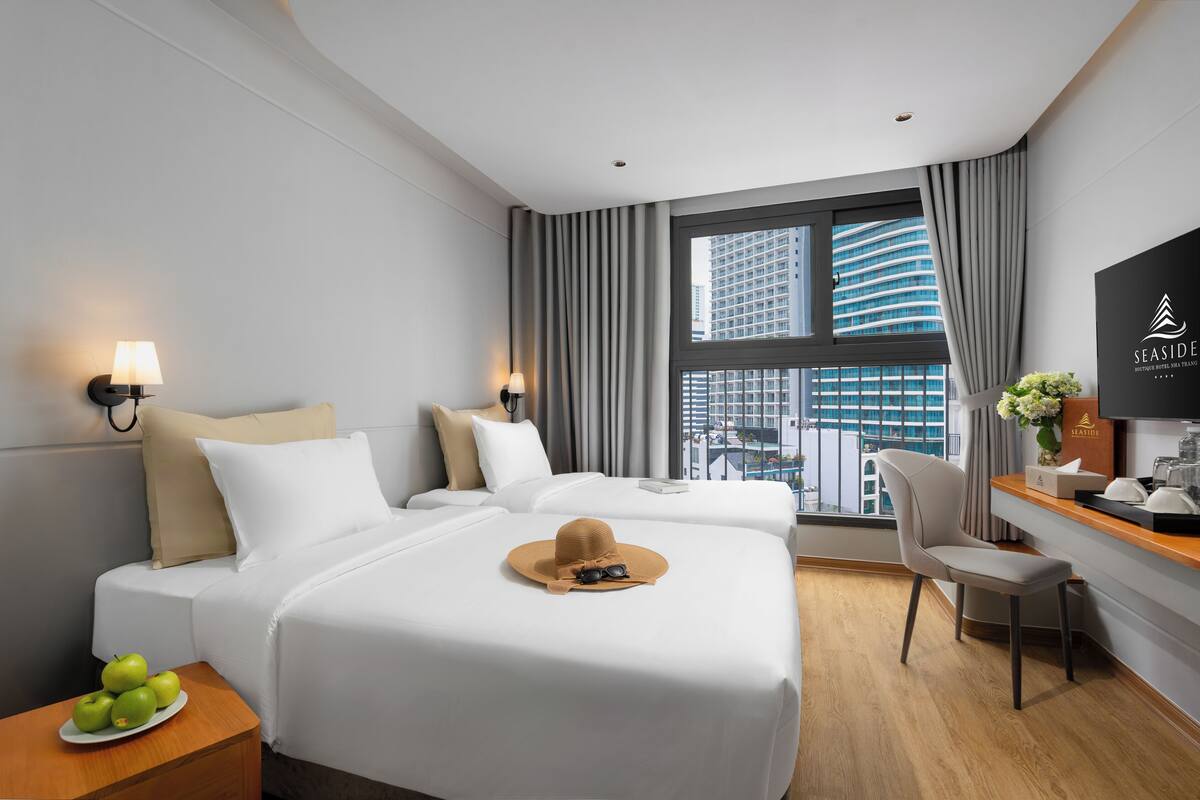 A hotel room with two beds, a desk, a chair, a TV, and a window with a city view.
