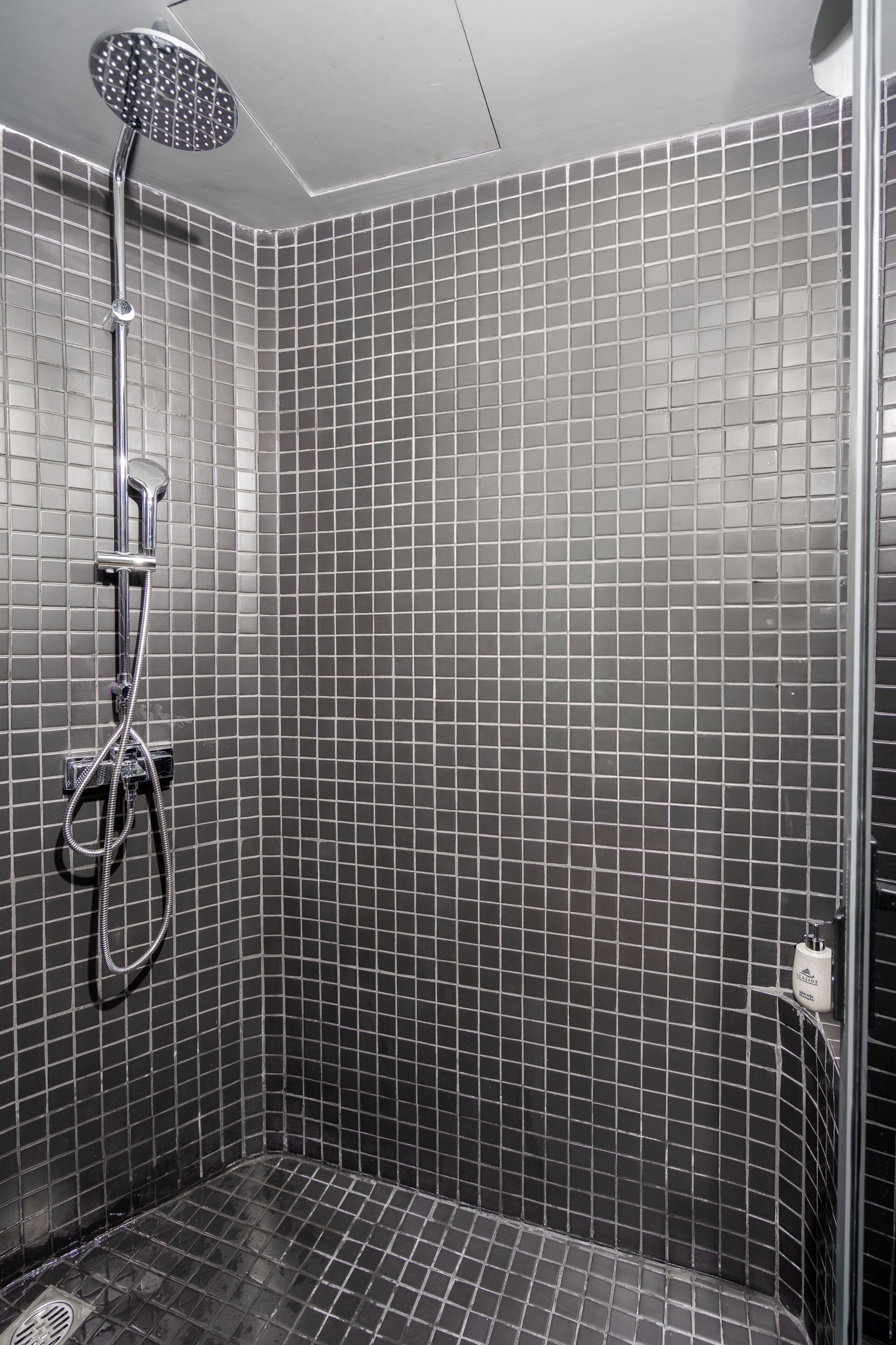 A shower with a handheld showerhead and a wall-mounted faucet.