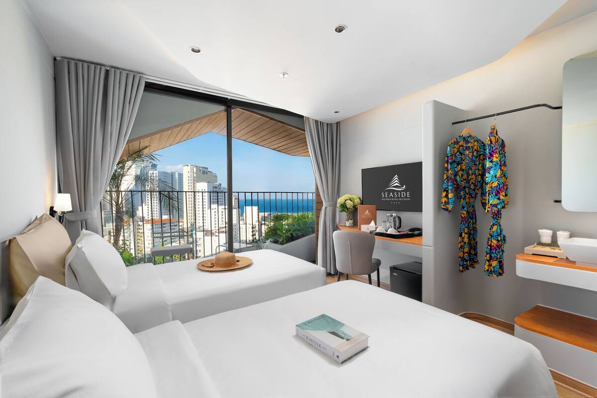 A modern hotel room with a large balcony, a desk, and a bed.
