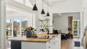 A modern kitchen with a wooden countertop, black pendant lights, and a large window overlooking a garden.