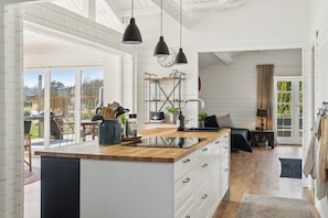 Una cocina moderna con encimera de madera, lámparas colgantes negras y un ventanal grande con vistas a un jardín.