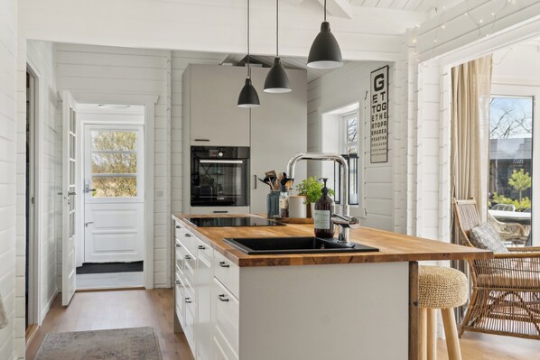 A modern kitchen with white cabinetry, a wooden island, pendant lighting, and a view to the outside.