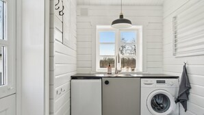 Een kleine wasserij met een wasmachine, een spoelbak en een raam.