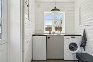 Een kleine wasserij met een wasmachine, een spoelbak en een raam.