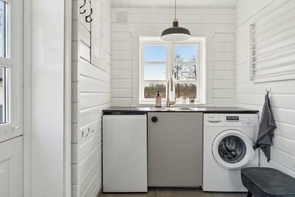 Une petite buanderie équipée d’un lave-linge, d’un évier et d’une fenêtre.