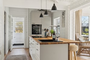 Una cocina moderna con armarios blancos, una isla de madera, iluminación colgante y vistas al exterior.
