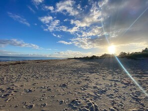 Une plage parsemée d’empreintes, un ciel dégagé et le soleil couchant.