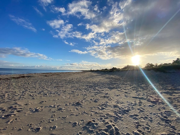 Una playa con huellas, cielo despejado y el sol poniéndose.