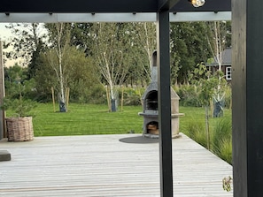 Un espace extérieur abrité comprenant un barbecue en pierre, une terrasse en bois et une pelouse.